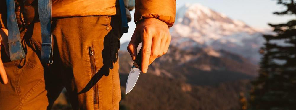 Hiker holding a knife against snowy peaks, showcasing essential gear for your next wild outdoor adventure.