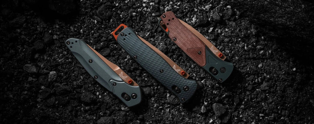 Three folding EDC knives with copper accents and textured handles rest on dark gravel, showcasing rugged design options.