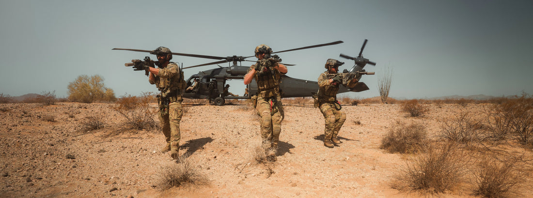 Three soldiers advance with rifles across a desert, black helicopter behind them, ready for tactical execution.
