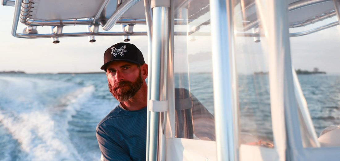 Bearded Captain Cody Chivas in a Nomad cap, looking back from his speeding boat on Florida waters.