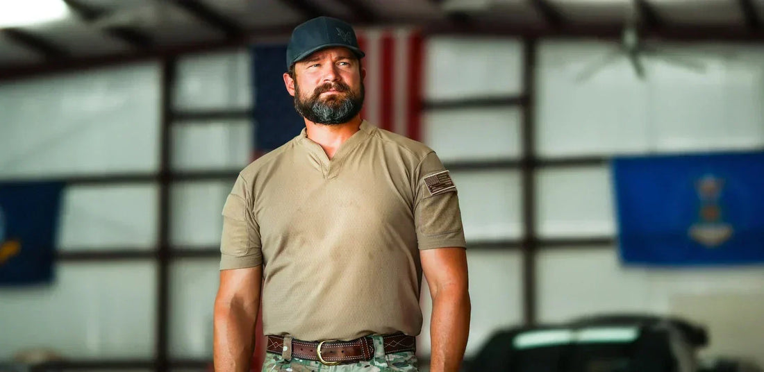 Bearded Darin Hardy in a tan shirt and cap stands resolutely before flags, embodying the rugged spirit of his mountain-inspired journey.