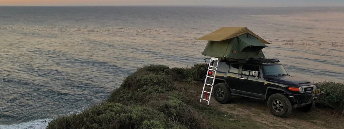 Black SUV with rooftop tent parked on a coastal cliff at dusk, capturing the spirit of reliable overlanding adventure.