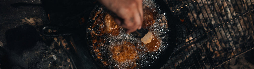 Lingcod pieces sizzle in bubbling oil within a cast-iron skillet, capturing the rustic warmth of outdoor cooking.