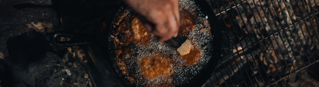 Lingcod pieces sizzle in bubbling oil within a cast-iron skillet, capturing the rustic warmth of outdoor cooking.