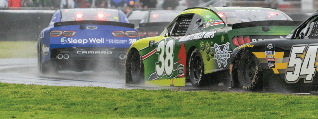 Rain-slicked NASCARs race side-by-side on a wet track, capturing the thrill and chaos of weekend competition.
