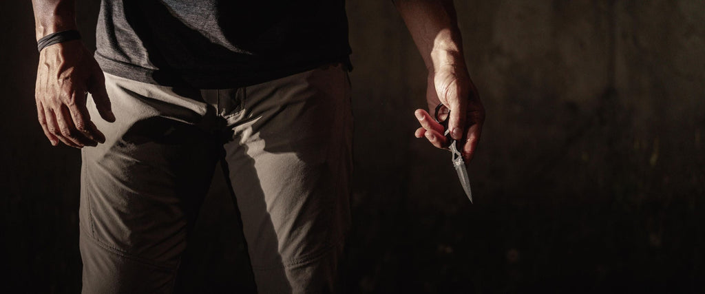 Person in tactical gear holds a Benchmade SOCP knife against a dark, moody background, ready for preparedness.