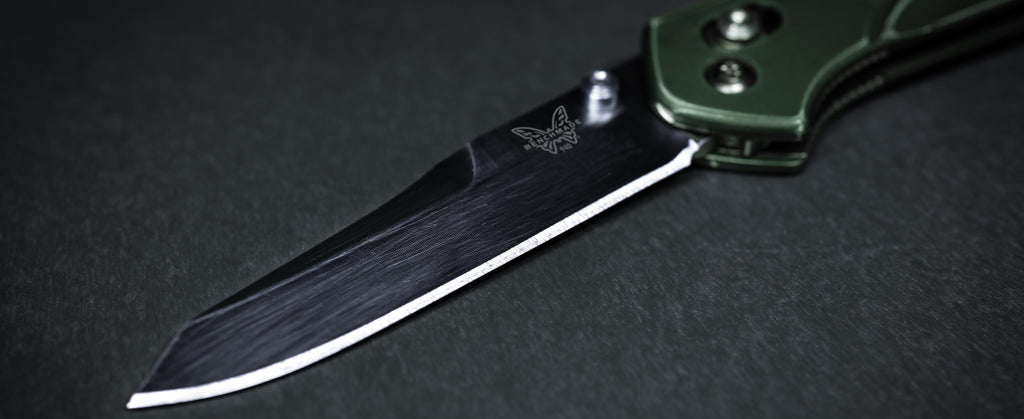 Close-up of a Benchmade folding knife with an olive handle and sharp blade on a dark textured surface.