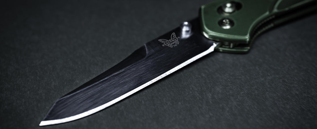 Close-up of a Benchmade folding knife with an olive handle and sharp blade on a dark textured surface.