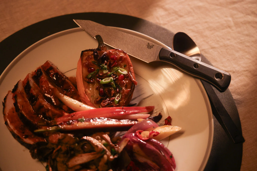 Sliced glazed carrots with sumac garnish on a plate beside a knife, in warm golden light.