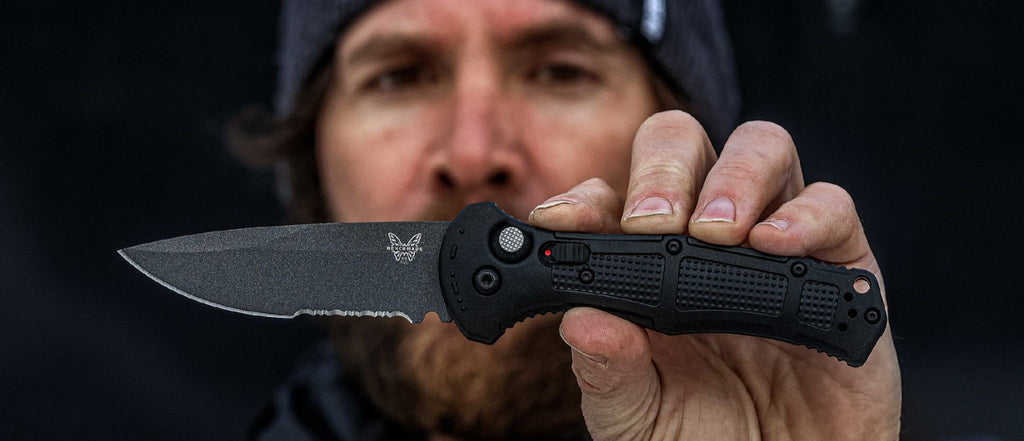Man holds black tactical folding knife with textured handle, showcasing grip design and blade against a dark background.