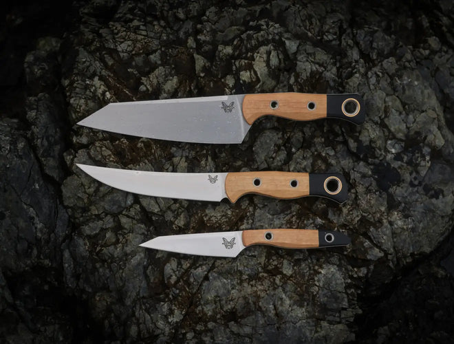 Three Benchmade knives with wood and black handles arranged on a dark, textured rock surface.