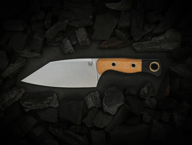 Benchmade fixed-blade knife with tan wood handle and silver blade rests on dark charcoal rocks.