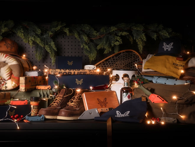 Benchmade gear display with boots, knives, hats, and boxes under warm string lights against evergreen garland.