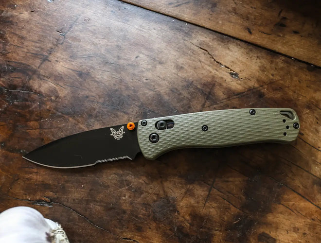 Benchmade folding knife with olive green handle and black blade rests on a scratched dark wooden table surface.