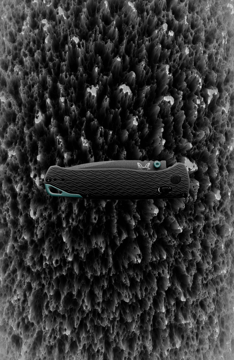 Closed black Benchmade folding knife with teal accents and textured grip lies on rough gray rock surface.
