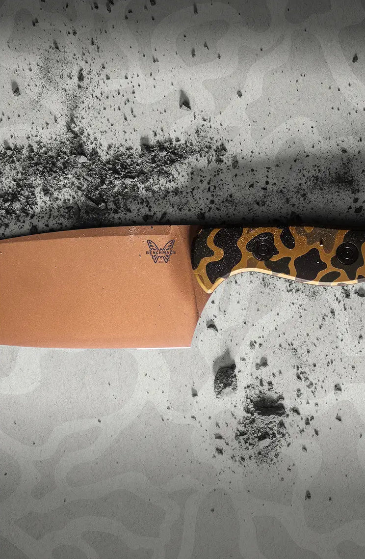 Benchmade knife with bronze blade and camouflage handle lies on a speckled gray surface.