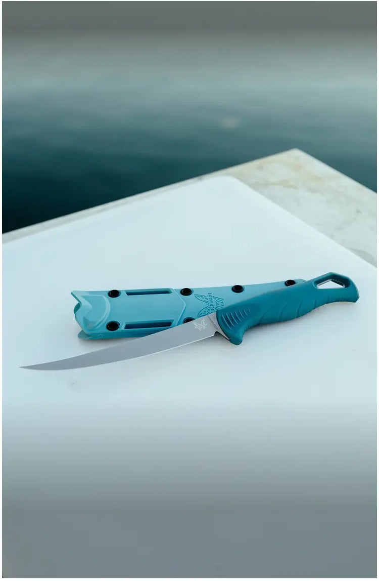 Teal-handled knife and sheath resting on a white surface near water, with "Benchmade" logo visible.