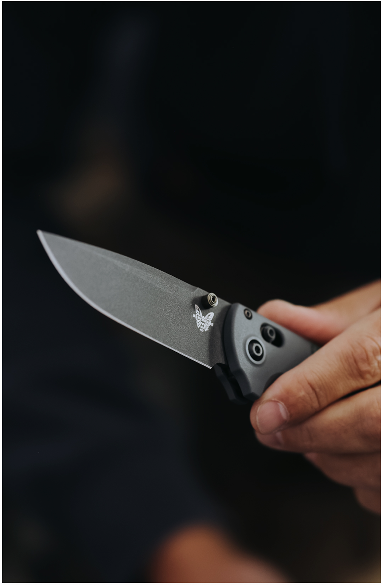Hand holds open gray Benchmade folding knife with butterfly logo against dark, blurred background.