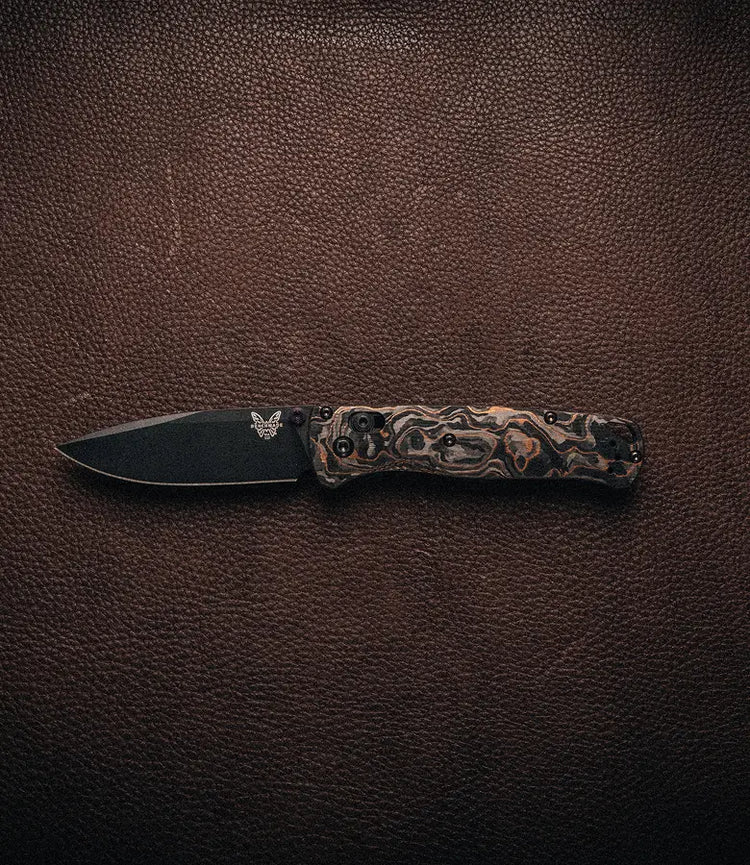 Folding knife with black blade and marbled handle rests on textured dark brown leather surface.