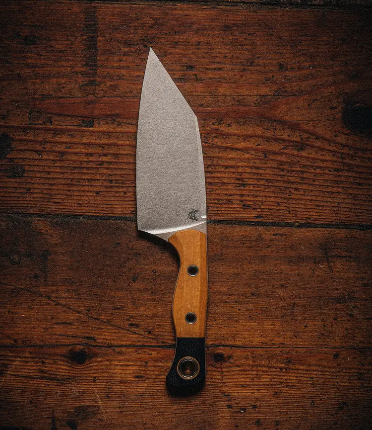 A fixed-blade knife with a light wooden handle and black lanyard rests on a dark, rustic wooden surface.