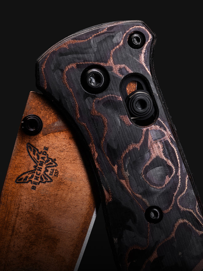 Close-up of a Benchmade folding knife with copper-patterned black handle and bronze blade, against a dark background.