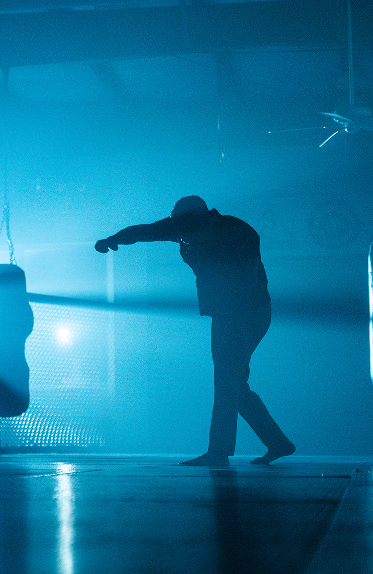 Silhouette of a person punching a hanging bag in a dimly lit, blue-hued gym.