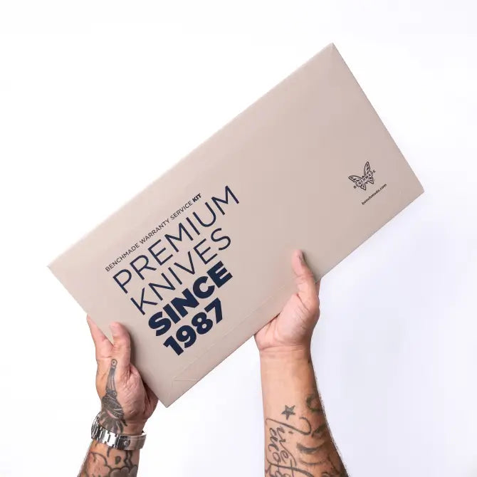 Tattooed hands hold a beige box titled "Premium Knives Since 1987" against a white background.