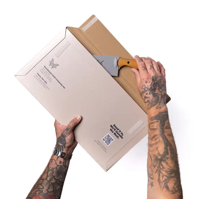 Tattooed hands use a knife to open a cardboard shipping box featuring the text "Send It In. We'll Handle The Rest."