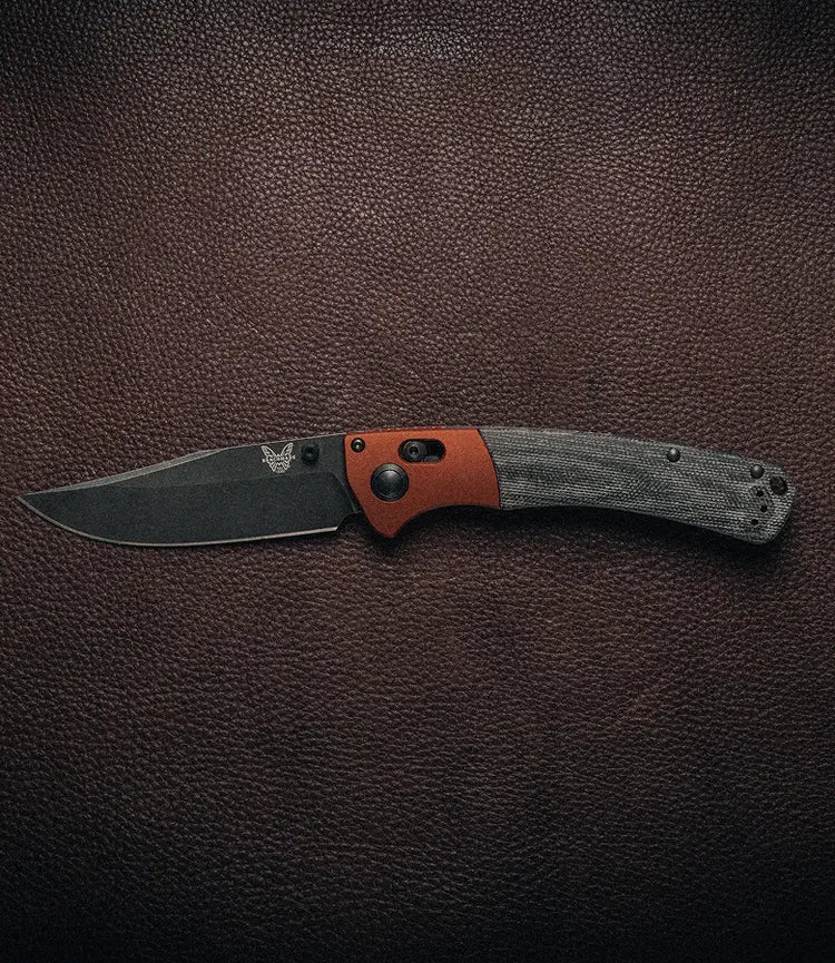 Folding knife with black blade, copper accent, and gray micarta handle rests on dark textured leather surface.