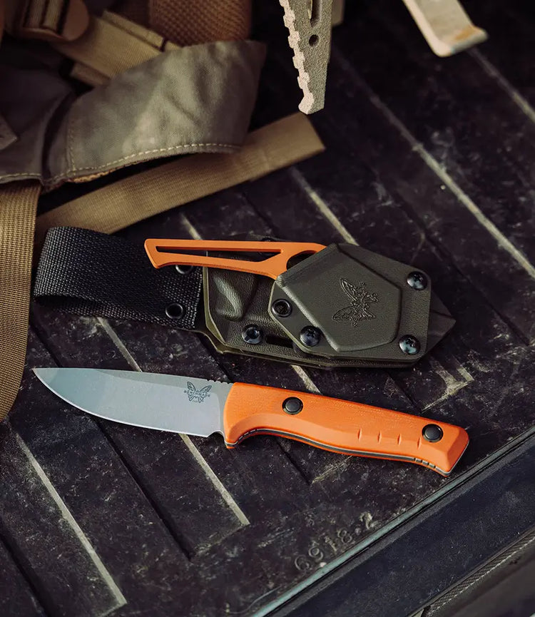 Orange-handled fixed-blade knife with matching sheath rests on a black textured surface.