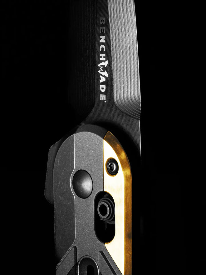 Close-up of a Benchmade folding knife with black and gold handle, set against a solid black background.