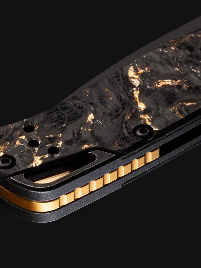 Close-up of a knife handle with black and gold marbled scales, brass liners, and a textured bronze backspacer.