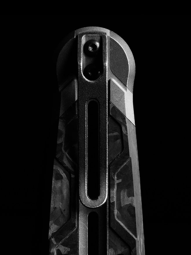Close-up of a tactical knife handle with carbon fiber scales and metal liner lock against a black background.