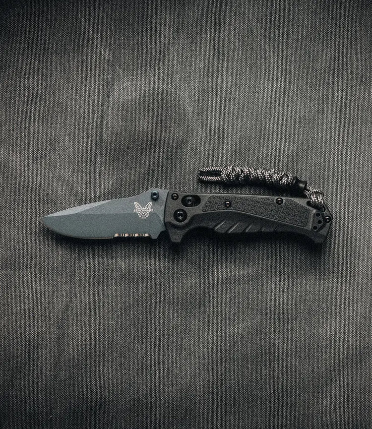 Black Benchmade folding knife with textured handle and paracord lanyard on gray fabric background.